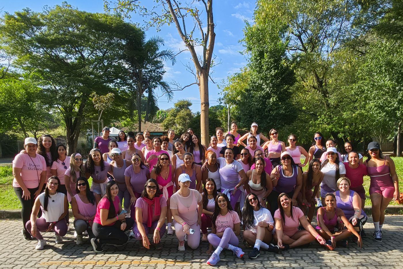 Encontro presencial da comunidade Power Wellness, com dezenas de mulheres de rosa e lilás num parque